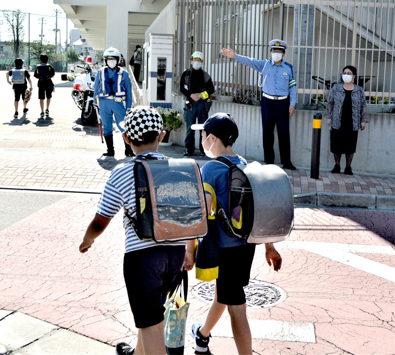 白バイ隊員らと一緒に船橋小の校門前に立ち、登校児童を見守る杵渕署長(右から2人目)と松本教育長(右)=27日朝、船橋市