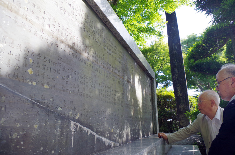 旧東金町が１９５２年に建立した縦１２０センチ・横２９６センチの「戦没英霊」の碑には満州事変から太平洋戦争までの２７６人の戦没者名が地域別に記載されている。碑文で戦禍を振り返る木村会長（左）と宇野さん＝東金市の八鶴湖畔専有地