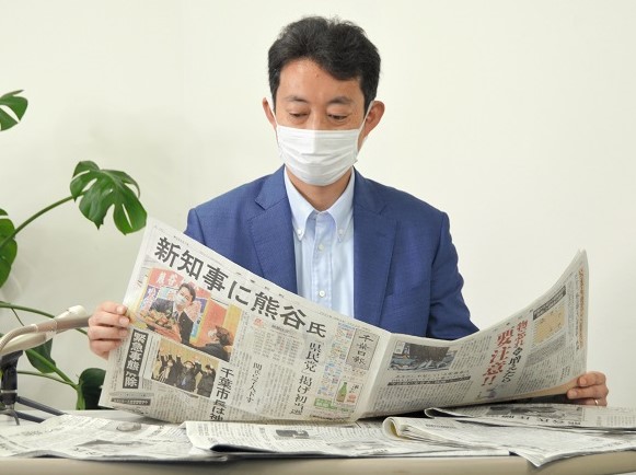 初当選から一夜明け、千葉県知事選を報じた千葉日報の記事に目を通す熊谷氏=22日朝、千葉市中央区の後援会事務所