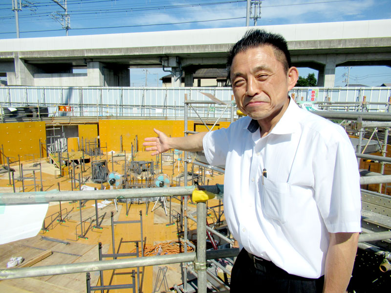 基礎部分が建設中の木造高層ビルと西峰社長。ビルの名前を「kinobiru」とつけた=鎌ケ谷市