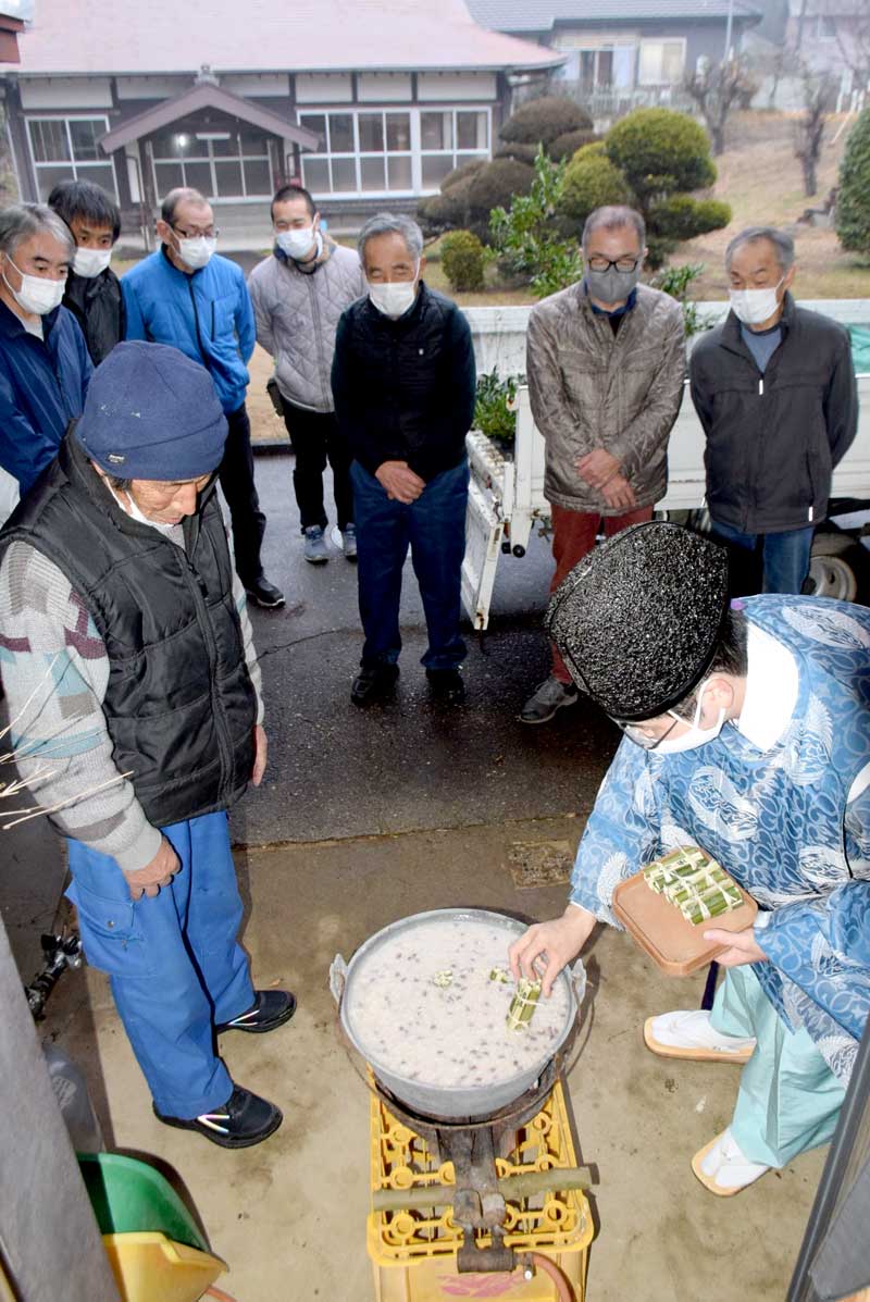 作物や月別の天候などの占い項目を記した青竹を鍋に入れる松山義仁宮司（右）＝匝瑳市の中台コミュニティーセンター