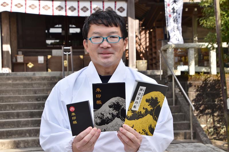 御朱印巡りに必要な神社案内帳と、オリジナルの御朱印帳を掲げる岡野さん=鴨川市