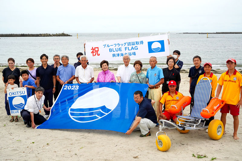 興津海水浴場でブルーフラッグを披露する照川市長(中央)ら=勝浦市