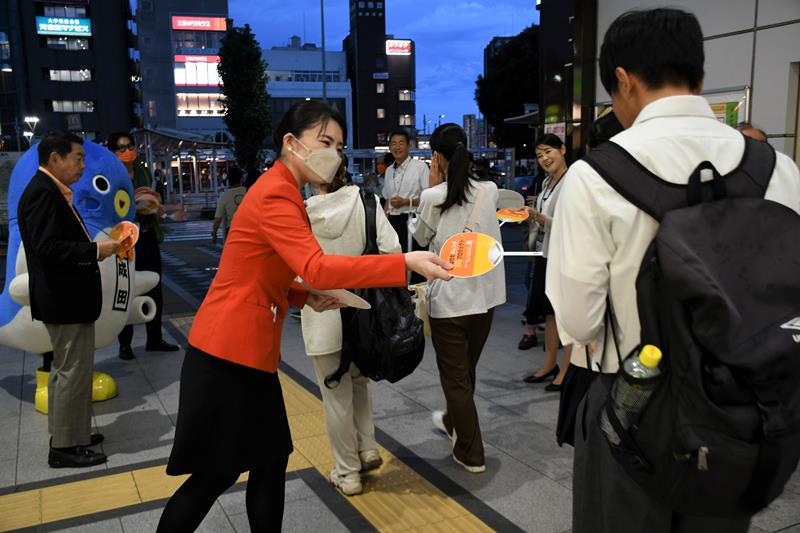 認知症理解への啓発カラーのオレンジ色の制服姿で啓発グッズを手渡す航空スタッフら=21日夜、成田市