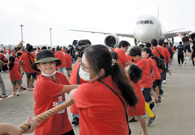 力を合わせ、巨大な航空機を楽しそうに引っ張る親子たち=17日、成田空港