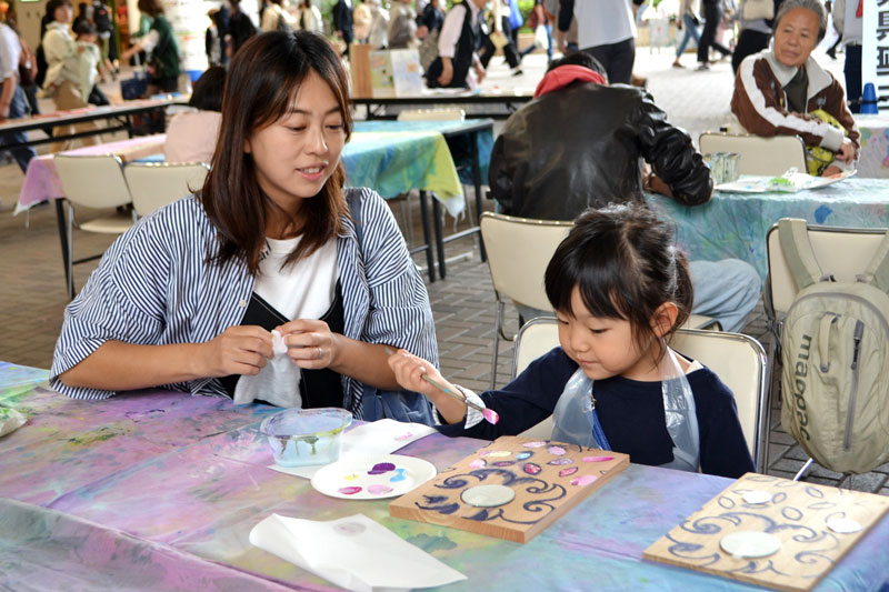 間伐材の板に絵の具で色をつける親子=千葉市中央区のそごう千葉店前広場