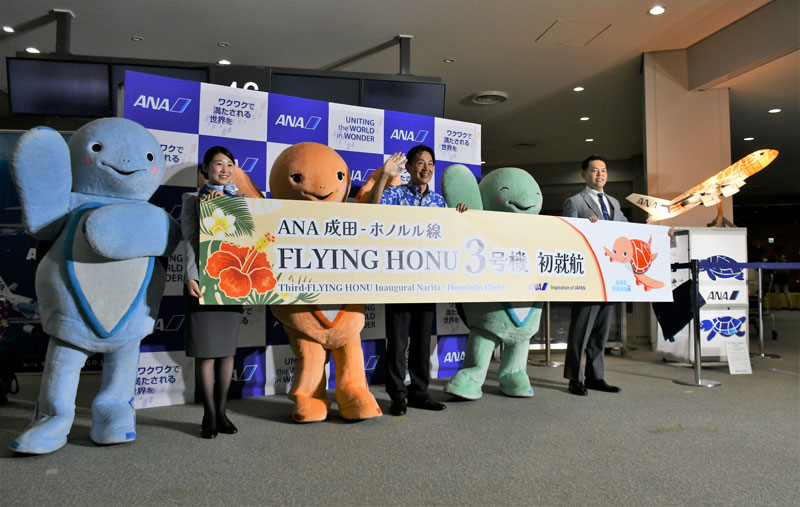 フライングホヌの3号機就航を祝うウミガメのマスコットキャラクターと岡支店長ら(中央)=20日夜、成田市の成田空港