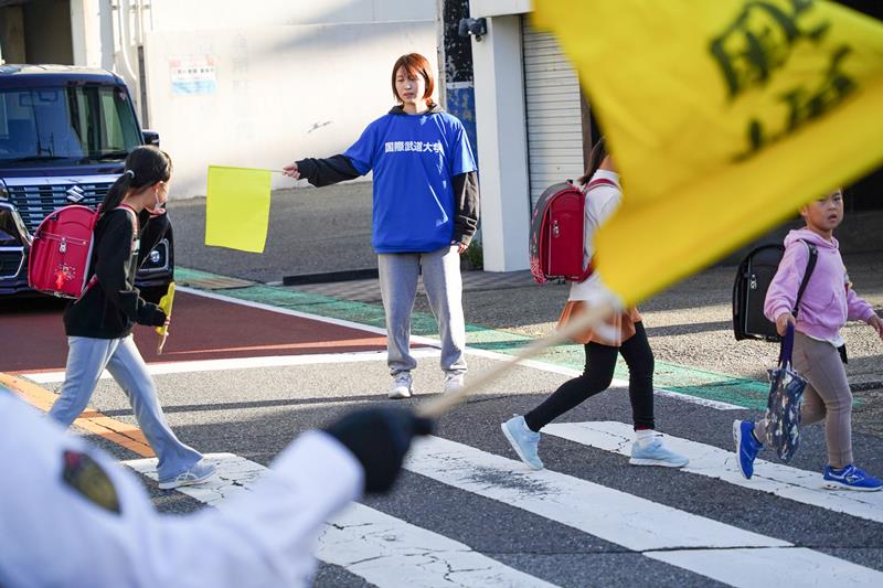 信号機のない横断歩道で登校する小学生を見守る国際武道大の学生=勝浦市