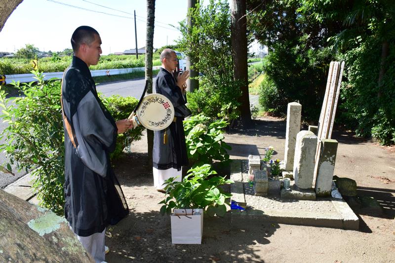 無縁塚津波精霊様の石碑の前でお経を唱える三橋潮倖住職(右)ら=8月21日、白子町