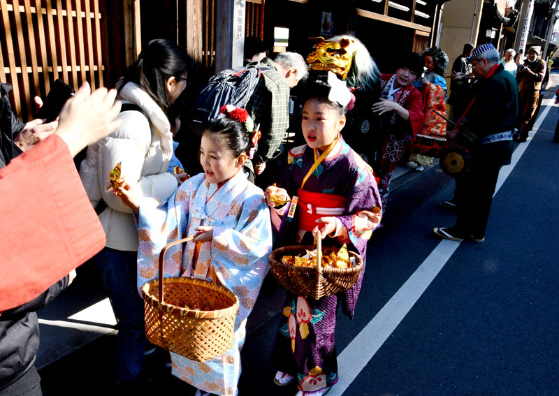 佐原の町並みに繰り出し、観光客らに折り鶴を配る子どもと獅子舞の一行