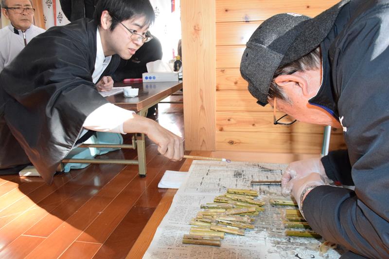 １本ずつ竹筒を割って米と小豆を確かめる松山宮司と氏子＝１５日、松山神社