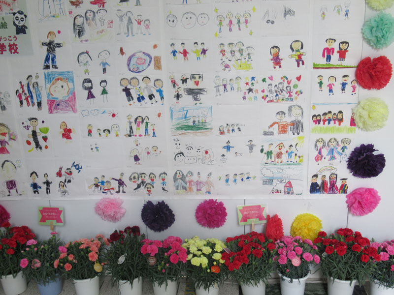 駅改札前に飾られた、近くの小学校などの子どもたちが描いた家族の絵。下はＪＡいちかわ寄贈のカーネーション＝３０日、市川市