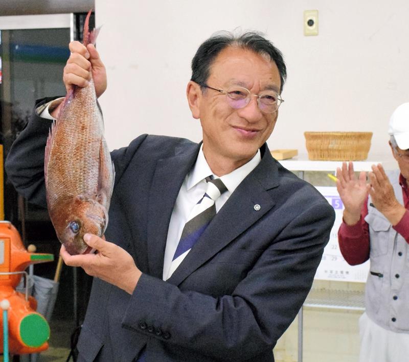 ３選を祝って届いたタイを掲げ、支援者と喜びを分かち合う馬淵氏＝１９日午後１０時５分ごろ、一宮町一宮の事務所