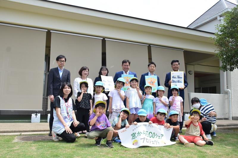 外付け日よけの前で記念撮影に応じる関係者と園児ら＝旭市