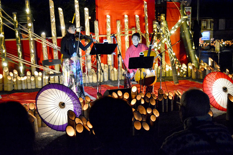 竹灯籠の明かりの前でバイオリンとチェロの二重奏が披露された=24日夜、勝浦市
