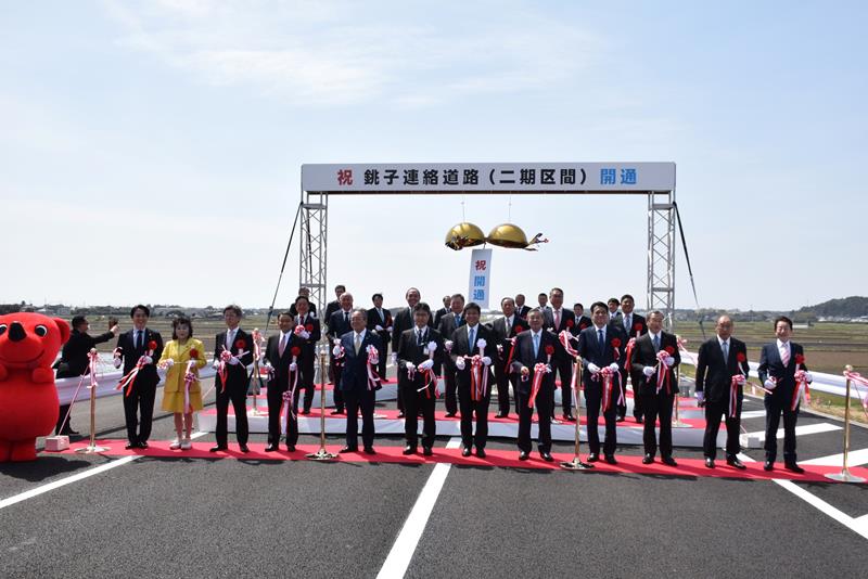 銚子連絡道路の新たな開通区間でテープカットとくす玉開きを行う関係者ら=3月31日、匝瑳市