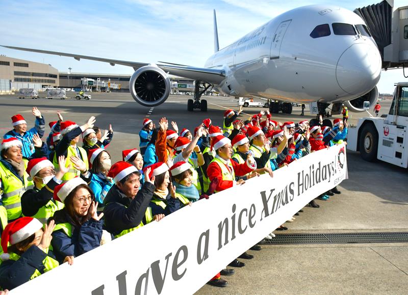 航空機に乗り込む旅客に向けて手を振るサンタ姿の成田空港スタッフら＝成田市