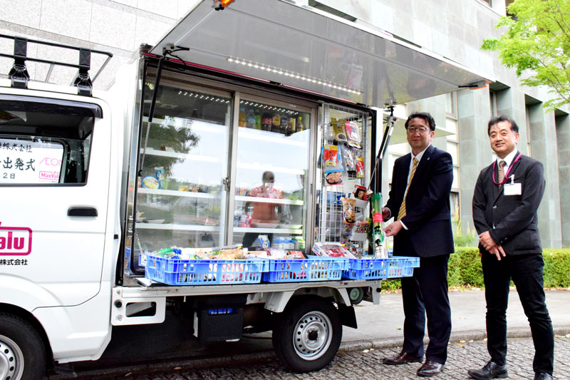 移動スーパーの出発式で商品を持つ月岡町長(左)とマックスバリュ関東の島田社長=22日、長柄町役場